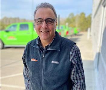 Male employee smiling in front of green trucks